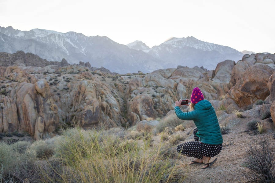 Woman in a Beanie Taking a Picture of Mountains with a Camera Phone