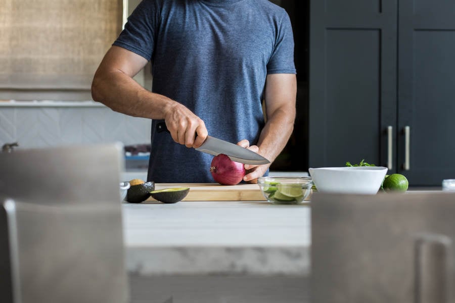 Man Slicing an Onion on a Wooden Cutting Board in a Kitchen
