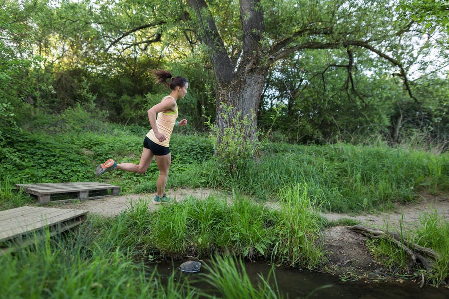 Young Athletic Woman Running on a Trail by a Creek