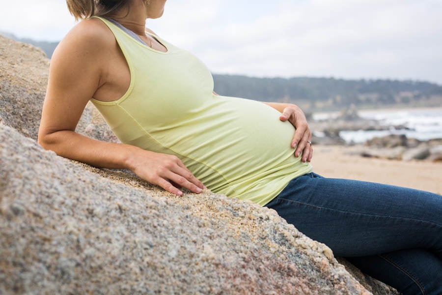 Pregnant Woman Sitting on a Rock on a Beach and Holding Her Belly