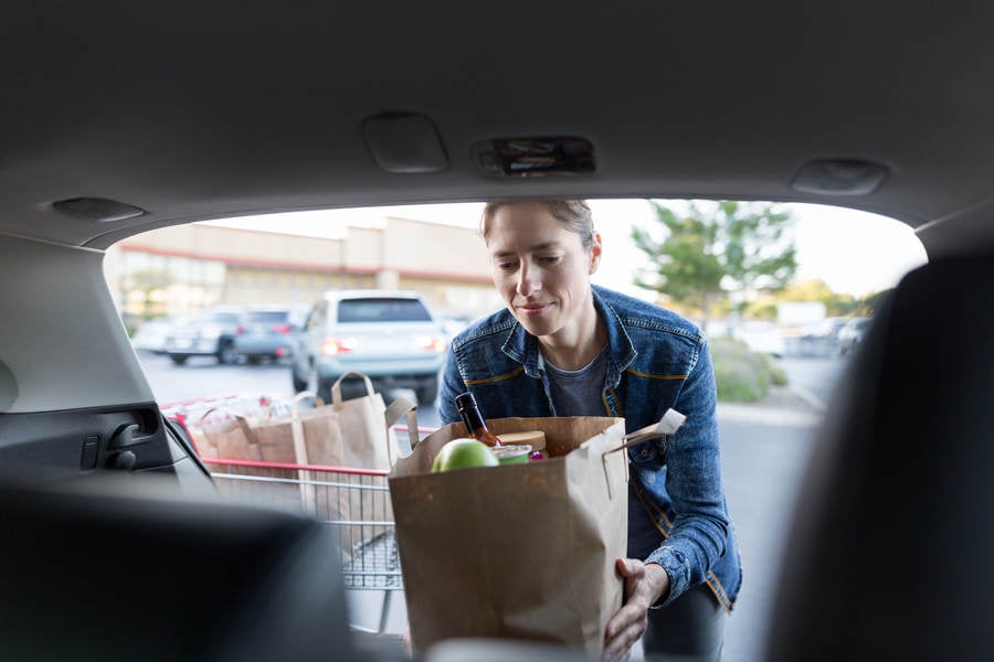 Woman Loading a Shopping Bag with Groceries in a Car Trunk