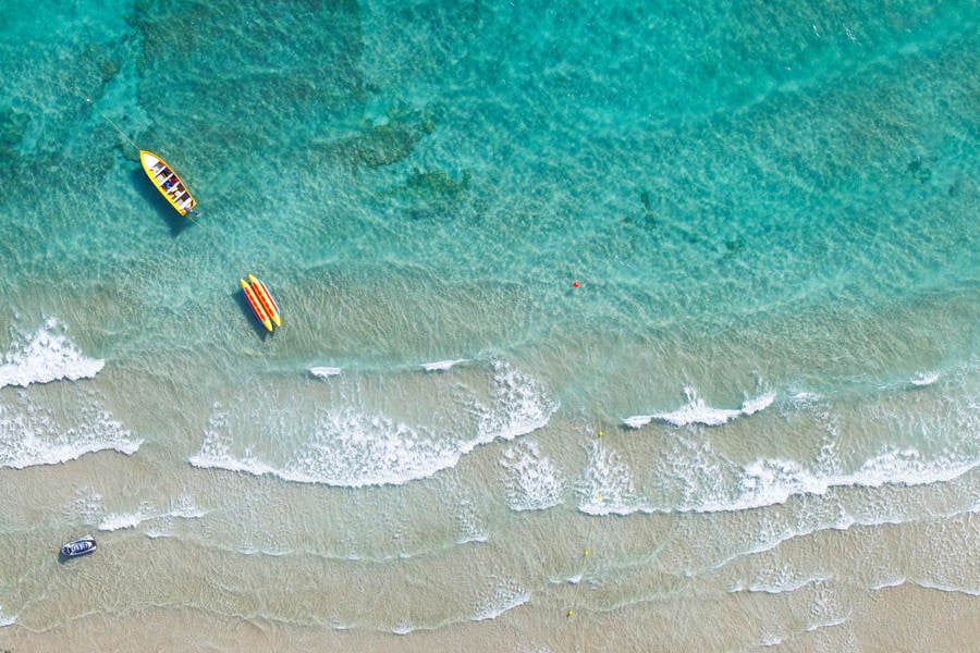 Aerial View of a Turquoise Sea Water with Boats and Waves Breaking