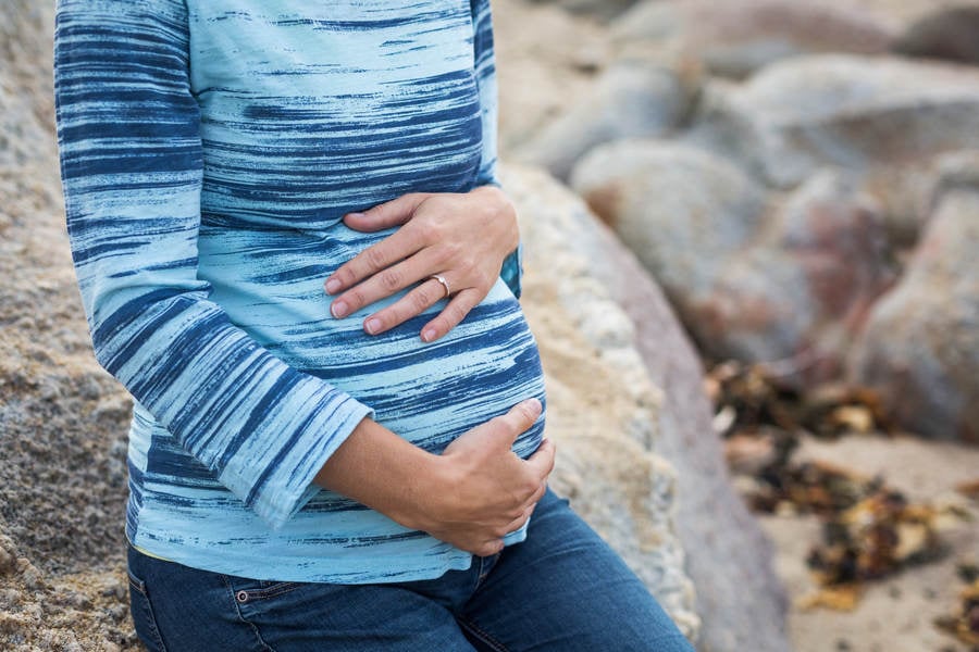 Close-Up of a Pregnant Woman Sitting on a Rock and Holding Her Bump
