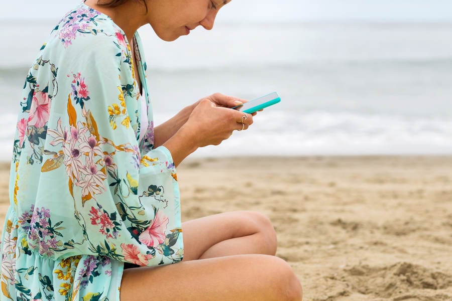 Young Woman Sitting on a Beach and Browsing on a Cell Phone