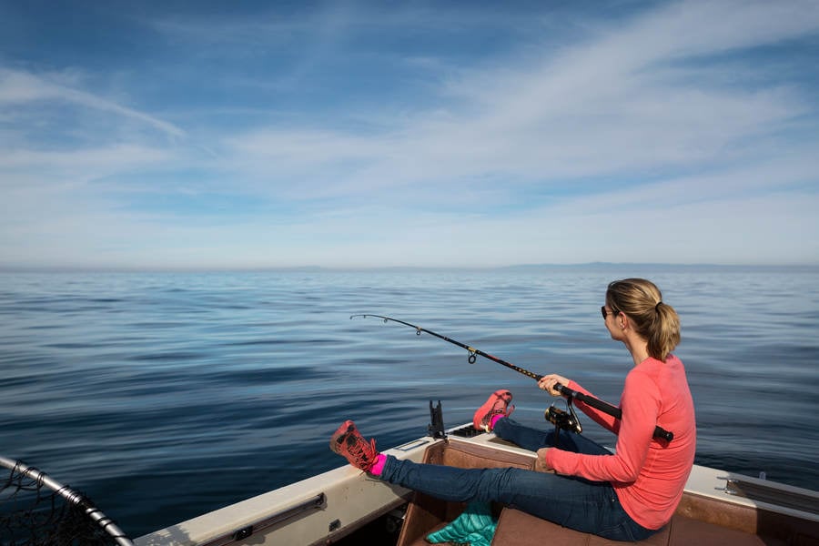 Young Woman Sitting in a Boat in a Calm Ocean and Fishing