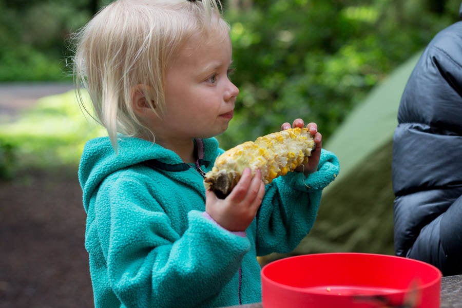 Toddler Girl Eating Corn on a Cob at a Campsite
