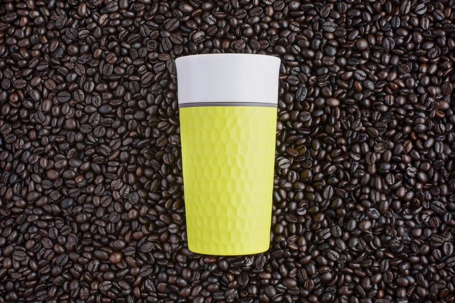 Two-Tone Fluorescent Yellow Coffee Travel Mug on a Background of Dark Roasted Coffee Bean