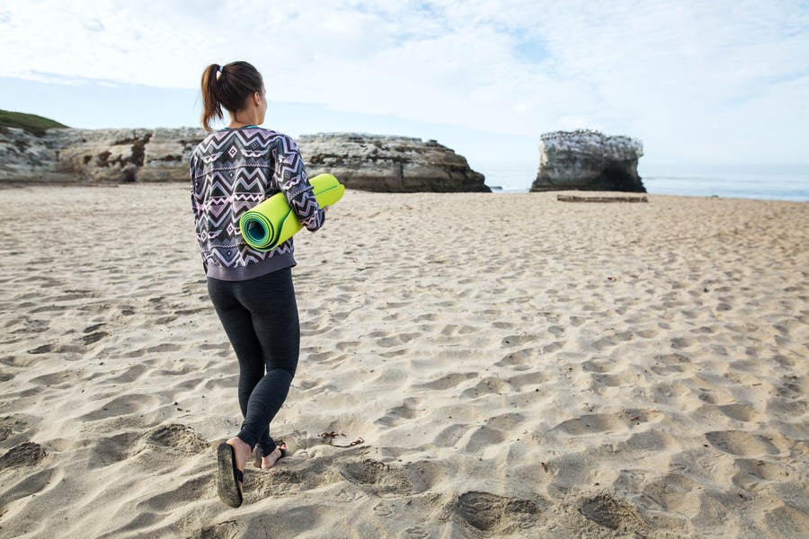 Girl with a Yoga Mat Walking on a Sandy Beach