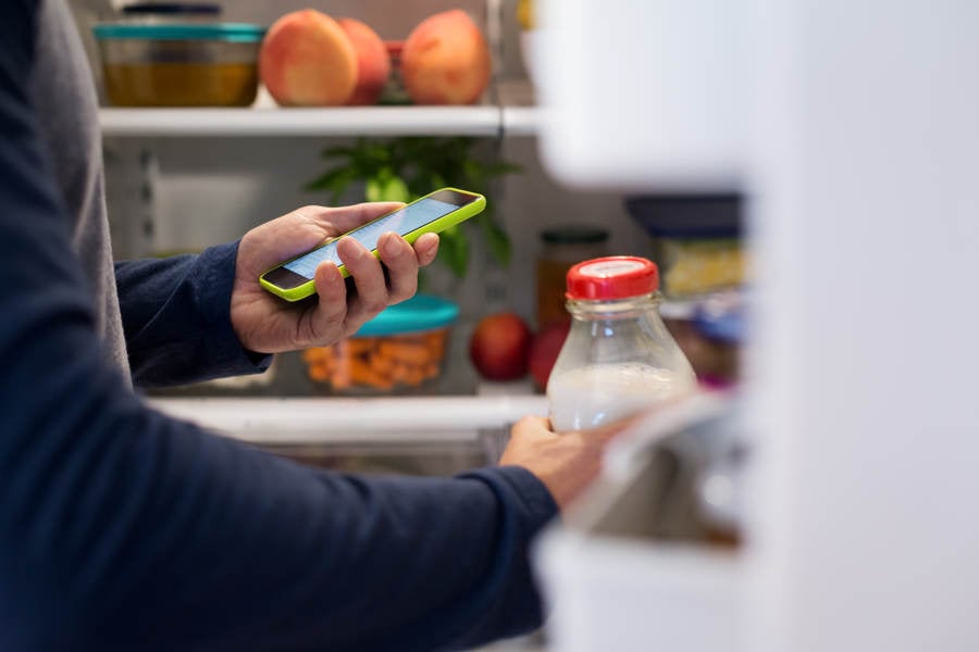 Man Looking at a Grocery Shopping List on a Cell Phone at a Refrigerator