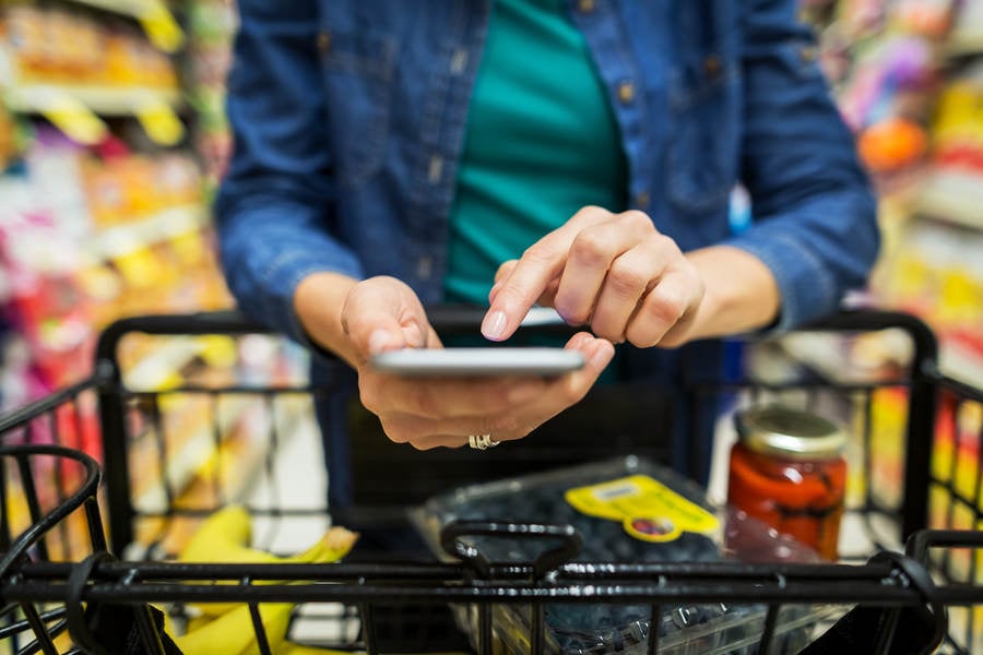 Close-Up of Woman with a Shopping Cart Researching Information on a Cell Phone