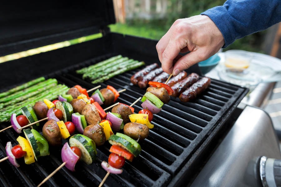 Man Grilling Vegetable Skewers and Sausages on a BBQ