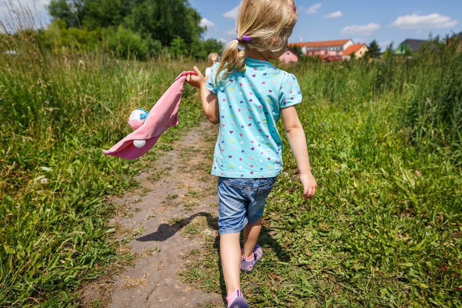 Rear View of a Little Girl Walking on a Trail Through Tall Grass