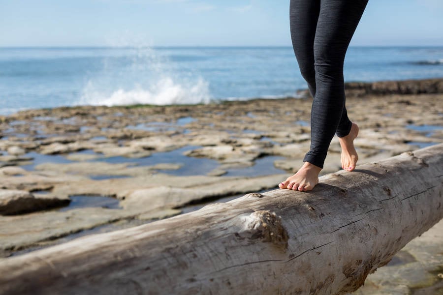 Low Section of a Woman Walking on a Tree Log on a Beach