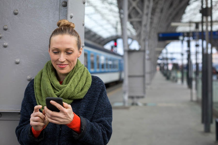 Smiling Woman Holding a Cell Phone on a Train Station Platform