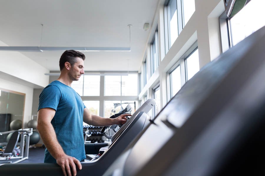 Man Selecting a Running Workout Setting on a Treadmill in a Gym