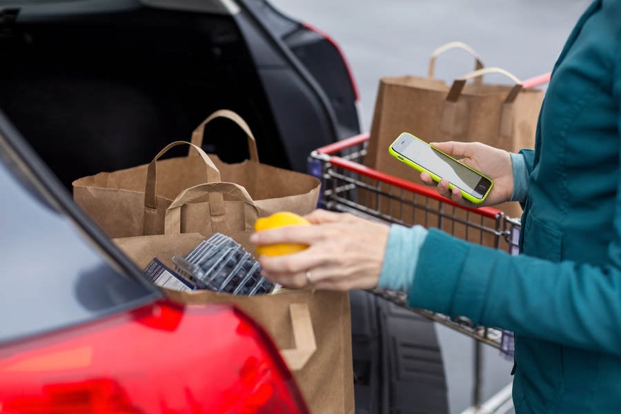 Woman Using a Smartphone and Arranging Bag with Groceries in a Car