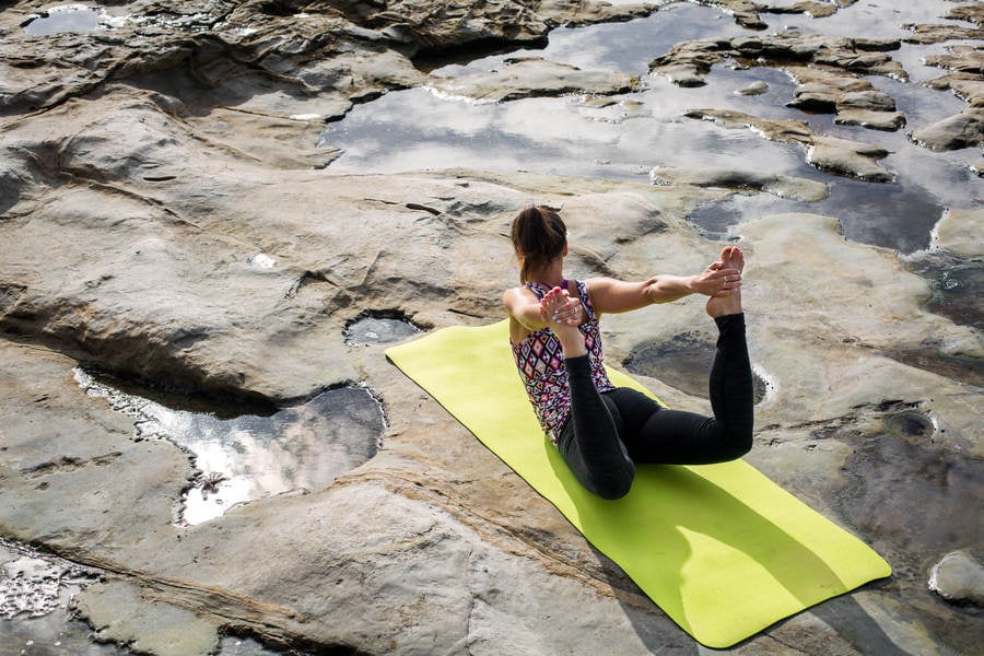 Young Woman Practicing Yoga Bow Pose by Tidal Pools