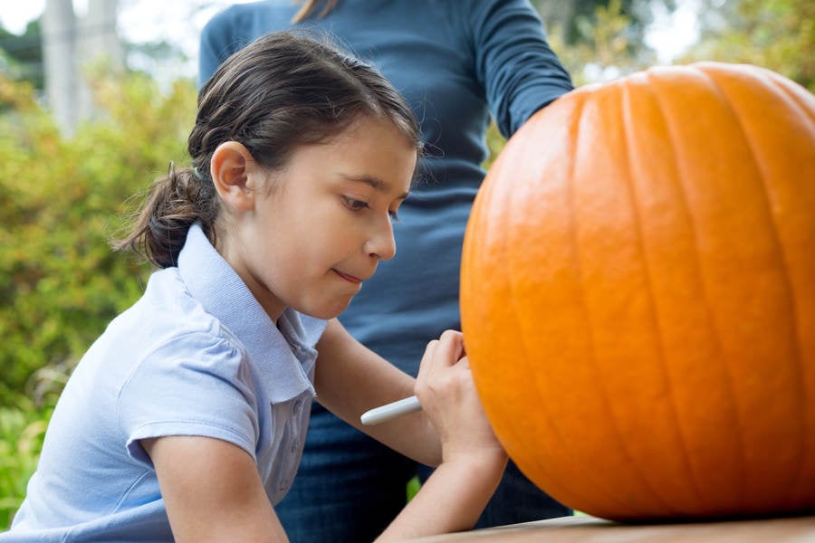 Young Girl Drawing on a Pumpkin with Her Mom
