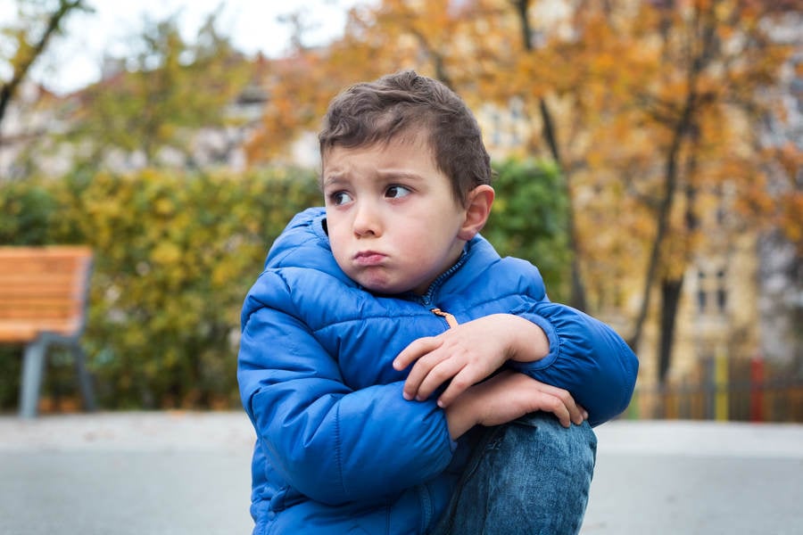 Frowning Little Boy Sitting on the Ground at a Public Park