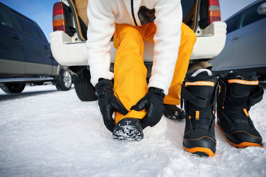 Man Putting on Snowboarding Boots at the Back of a Car