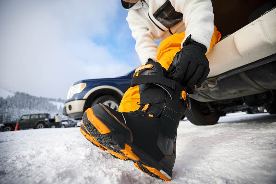 Ground-Level View of a Man Putting on Snowboarding Boots at a Parking Lot