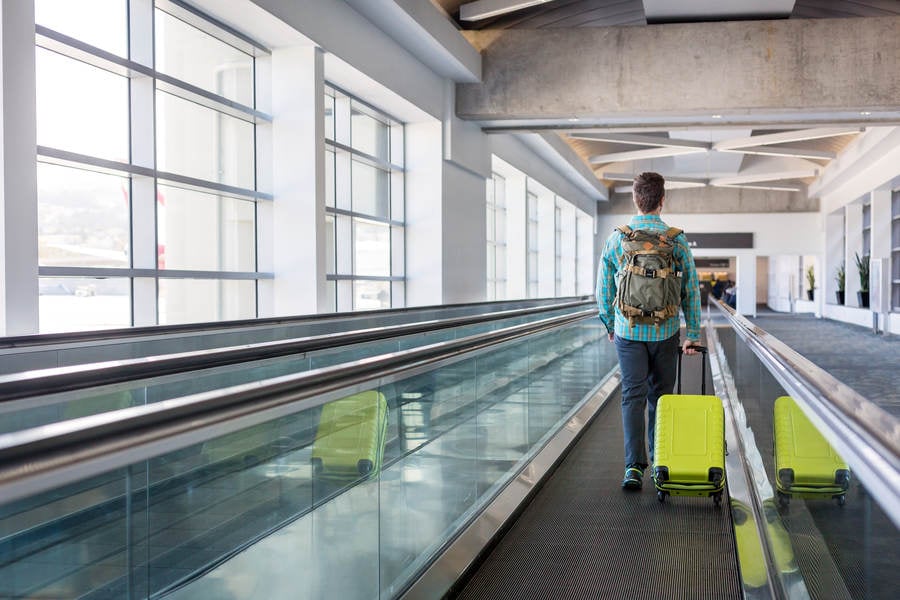 Traveler with a Luggage Walking on a Moving Walkway at an Airport Corridor