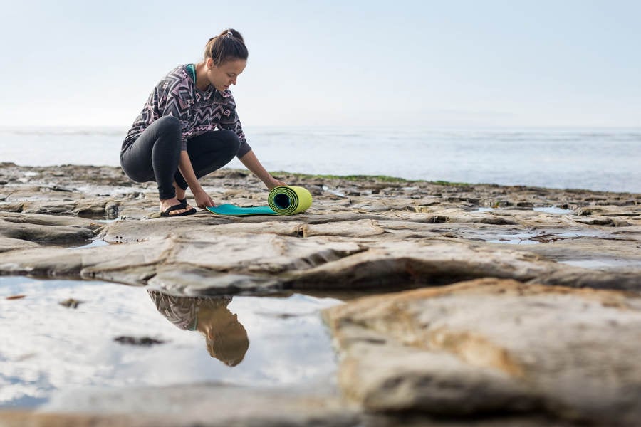 Young Athletic Woman Rolling a Yoga Mat on a Rocky Beach