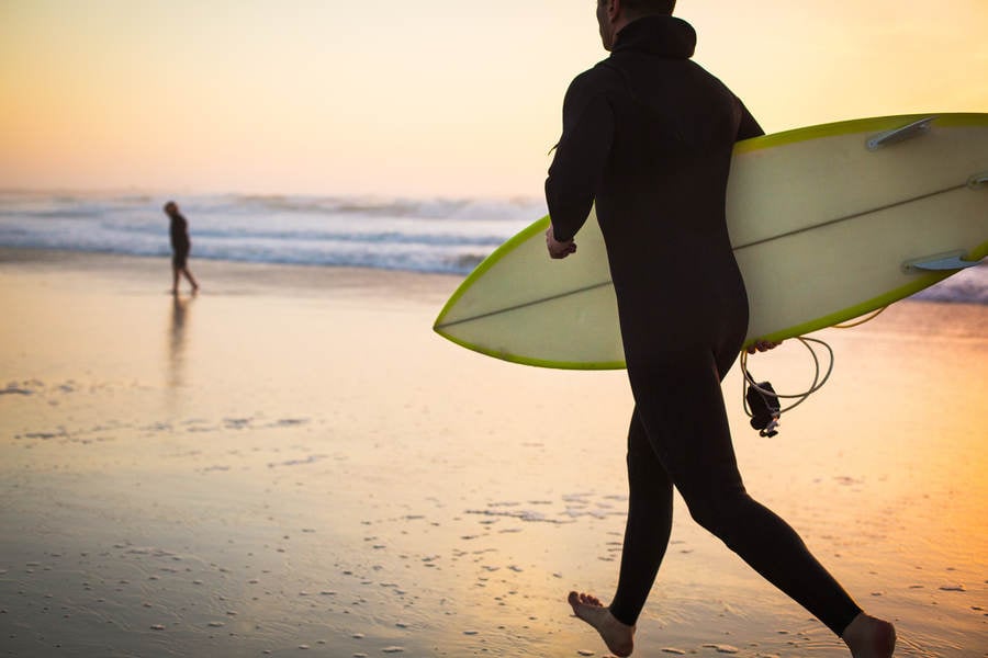 Man Holding a Surfboard Running on a Beach During Sunset