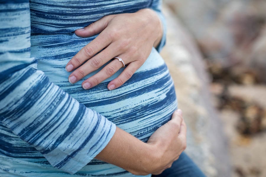 Close-Up of a Pregnant Woman Sitting on a Rock and Holding Her Belly