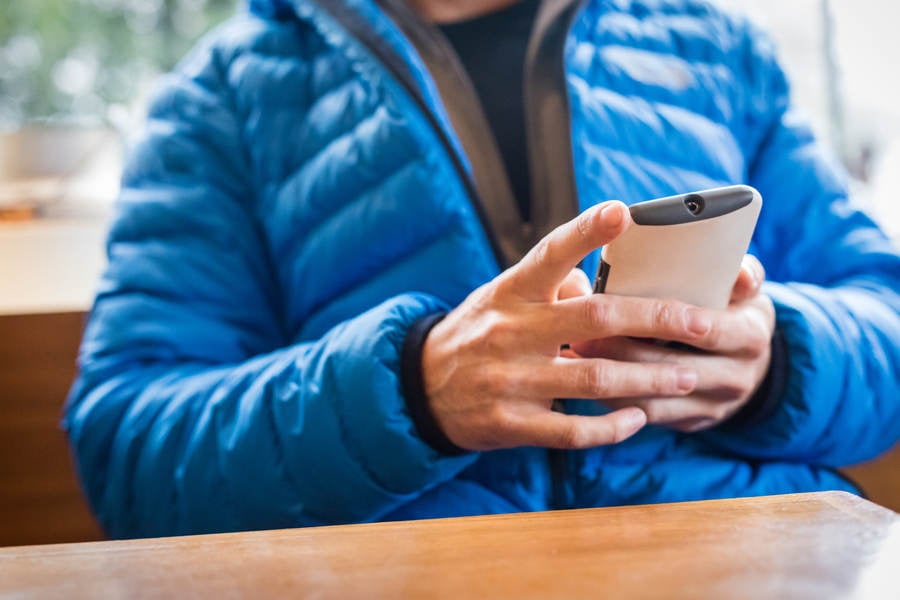 Man in a Down Jacket Sitting at a Coffee Shop and Looking at His Smartphone