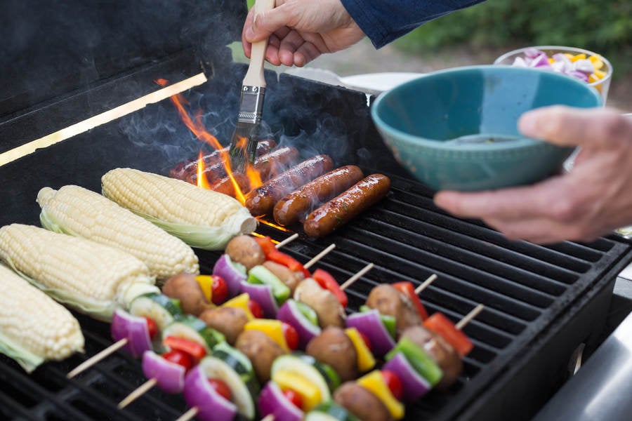 Man Braising Sausages on a Barbecue Grill with a Brush