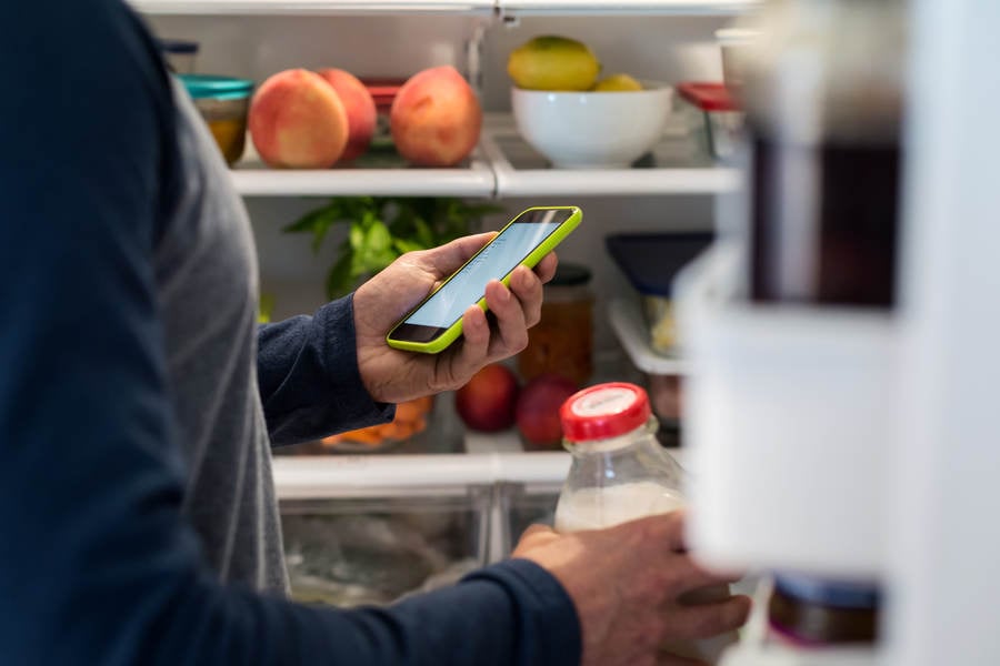 Man Looking at a Grocery Shopping List on a Smartphone at a Refrigerator