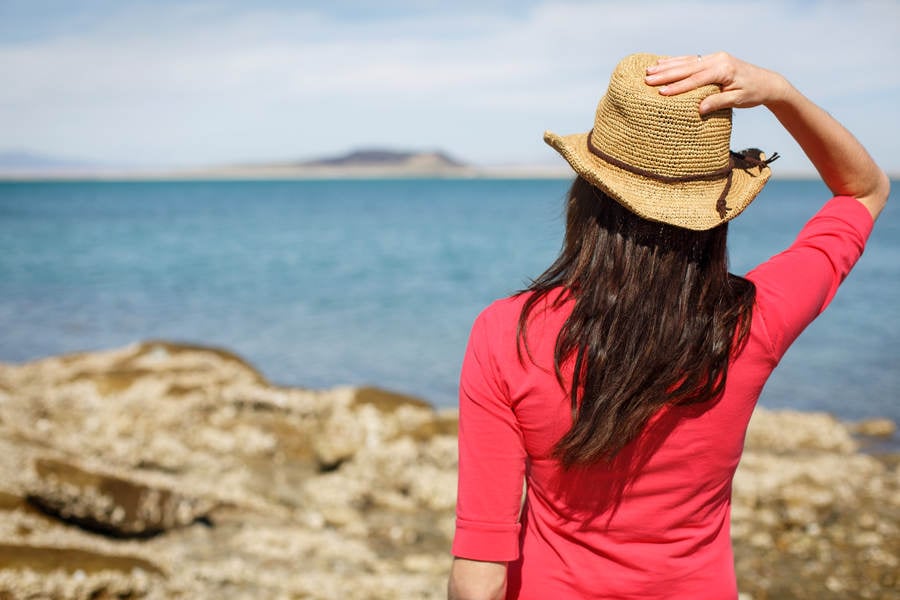 Girl in a Straw Hat Standing on a Coast Looking into Distance