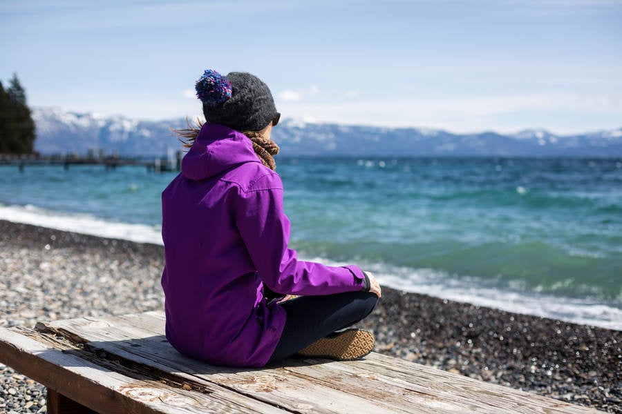 Woman in Winter Gear Sitting by an Alpine Lake and Contemplating