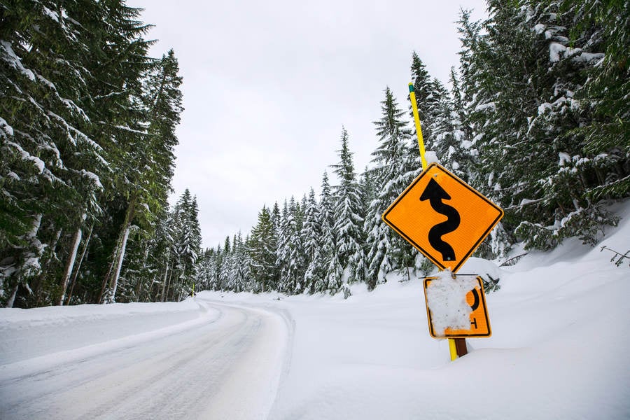 Low-Angle View of a Winding Road Sign Alongside a Snow-Covered Mountain Road