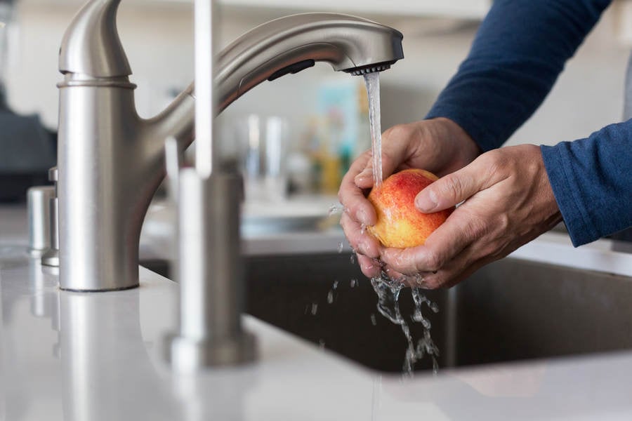 Man's Hands Rinsing an Apple under a Faucet in a Modern Kitchen
