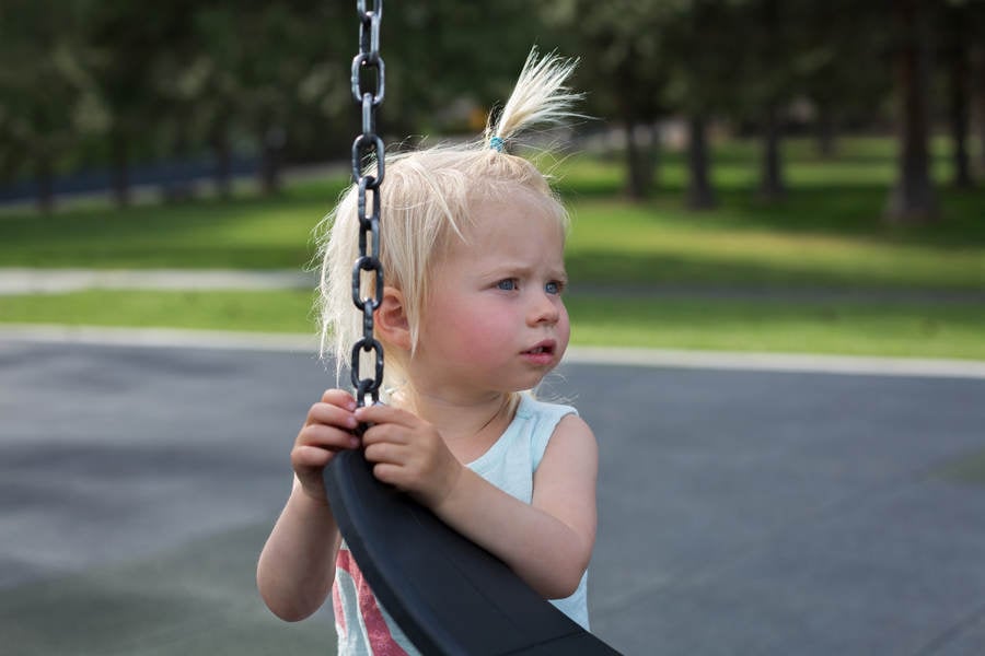 Toddler Girl Standing by a Swing at a Playground and Contemplating