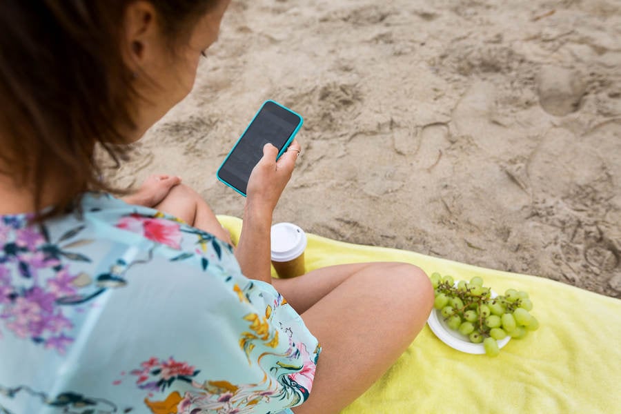 Young Woman With a Cell Phone Sitting on a Beach Towel