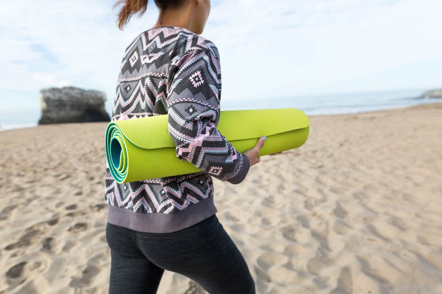 Young Athletic Woman with a Yoga Mat Walking on a Beach