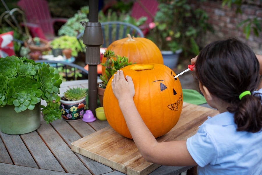 Young Girl Carving a Pumpkin on a Table