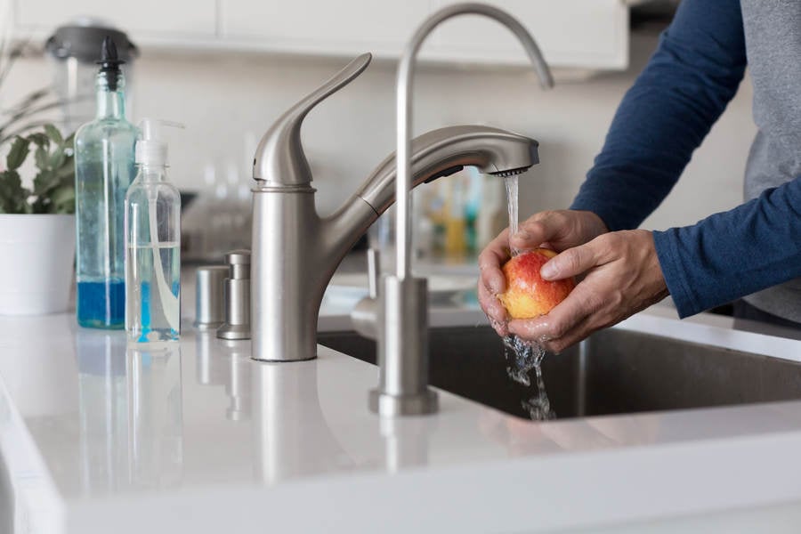 Man Rinsing an Apple under a Faucet in a Modern Kitchen