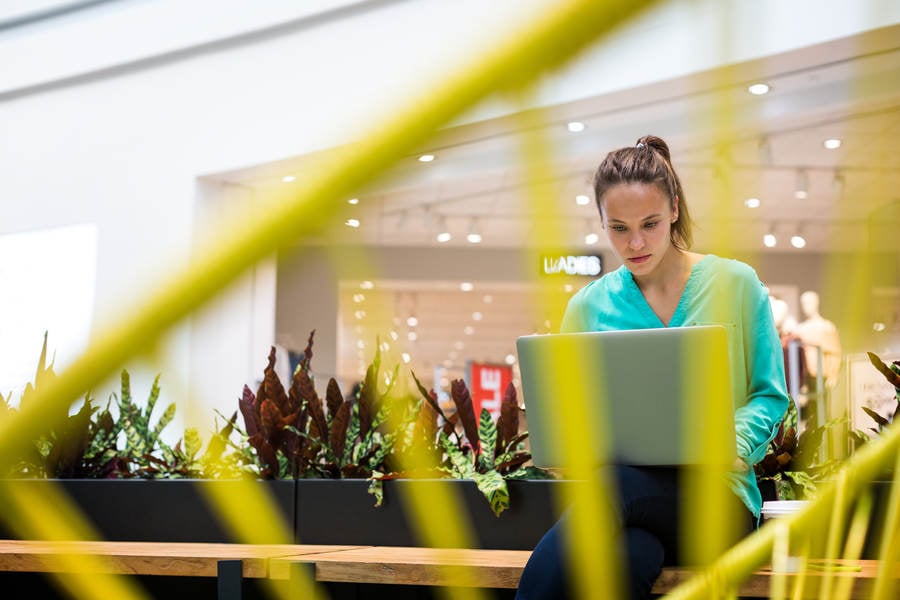 Woman Sitting on a Bench in a Shopping Mall and Using a Laptop