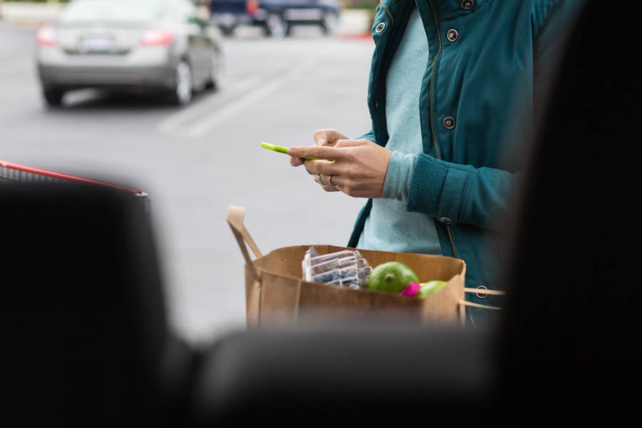 Woman Typing on a Cell Phone and Standing by a Car and a Shopping Cart