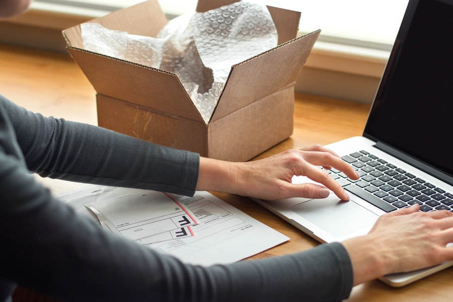 Woman Typing on a Laptop While Preparing Shipping Labels