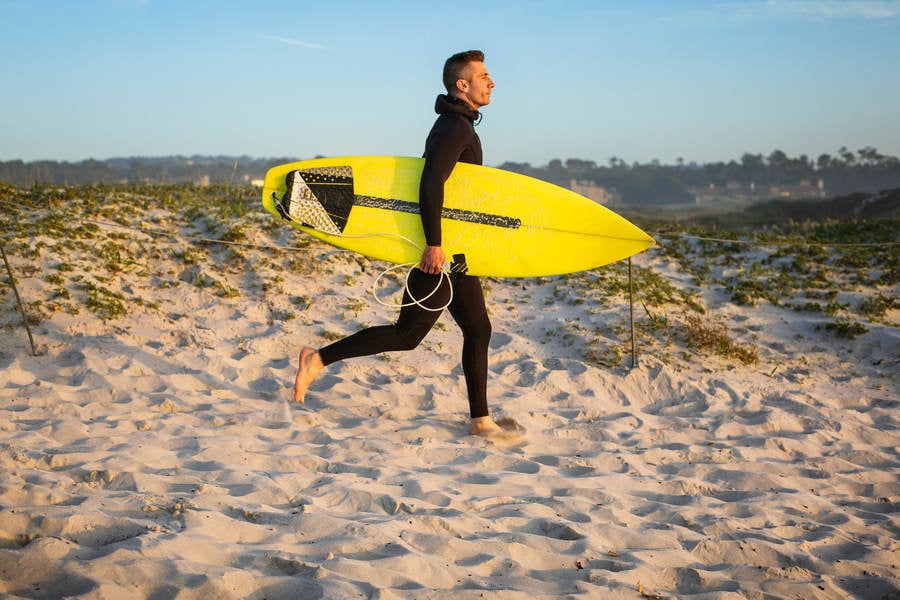 Male Surfer Running to a Beach While Carrying a Surfboard