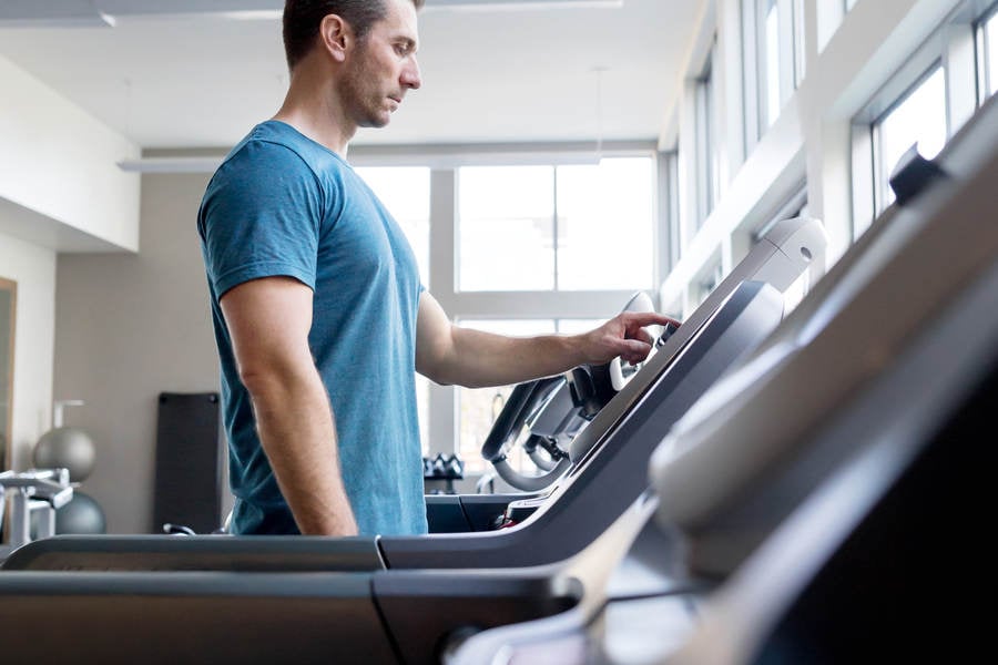 Man Selecting a Workout Setting on a Treadmill in a Fitness Gym