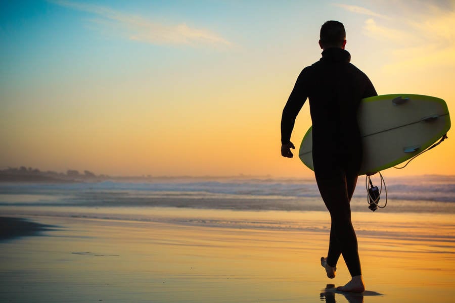 Male Surfer with a Surfboard Walking on a Beach During Sunset