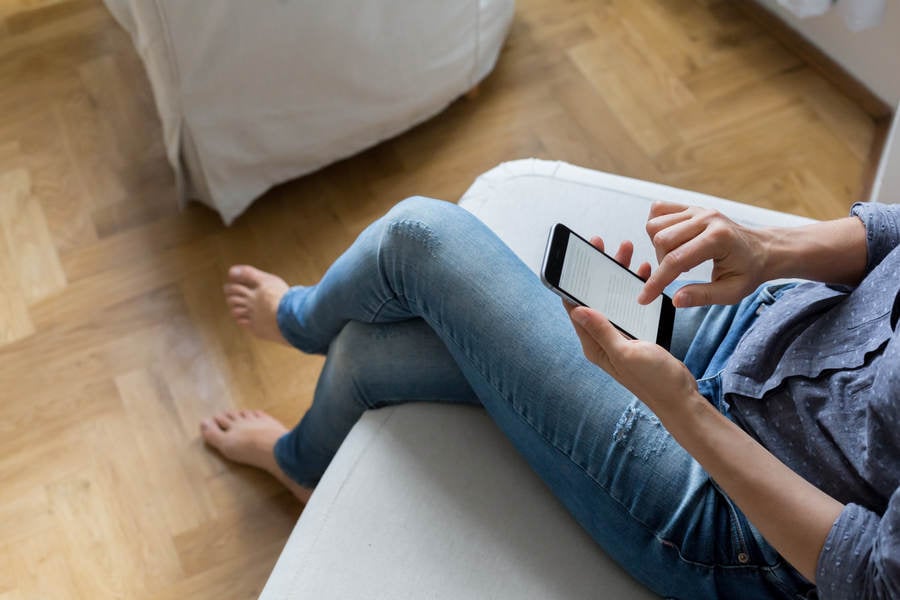 Young Woman Sitting on a Sofa at Home Using a Smartphone