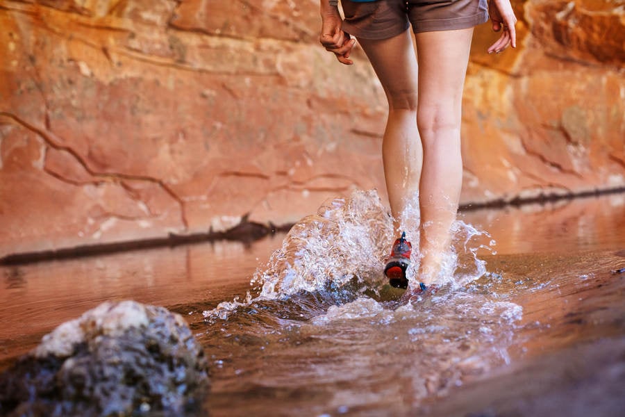 Low-Angle View of a Girl Hiking Through a Water by a Sandstone Wall