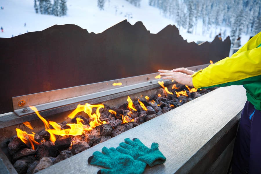Woman Warming Her Hands by a Fire Pit at a Ski Resort